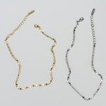 Delicate gold and silver dainty chain ankle bracelets side by side on a plain background