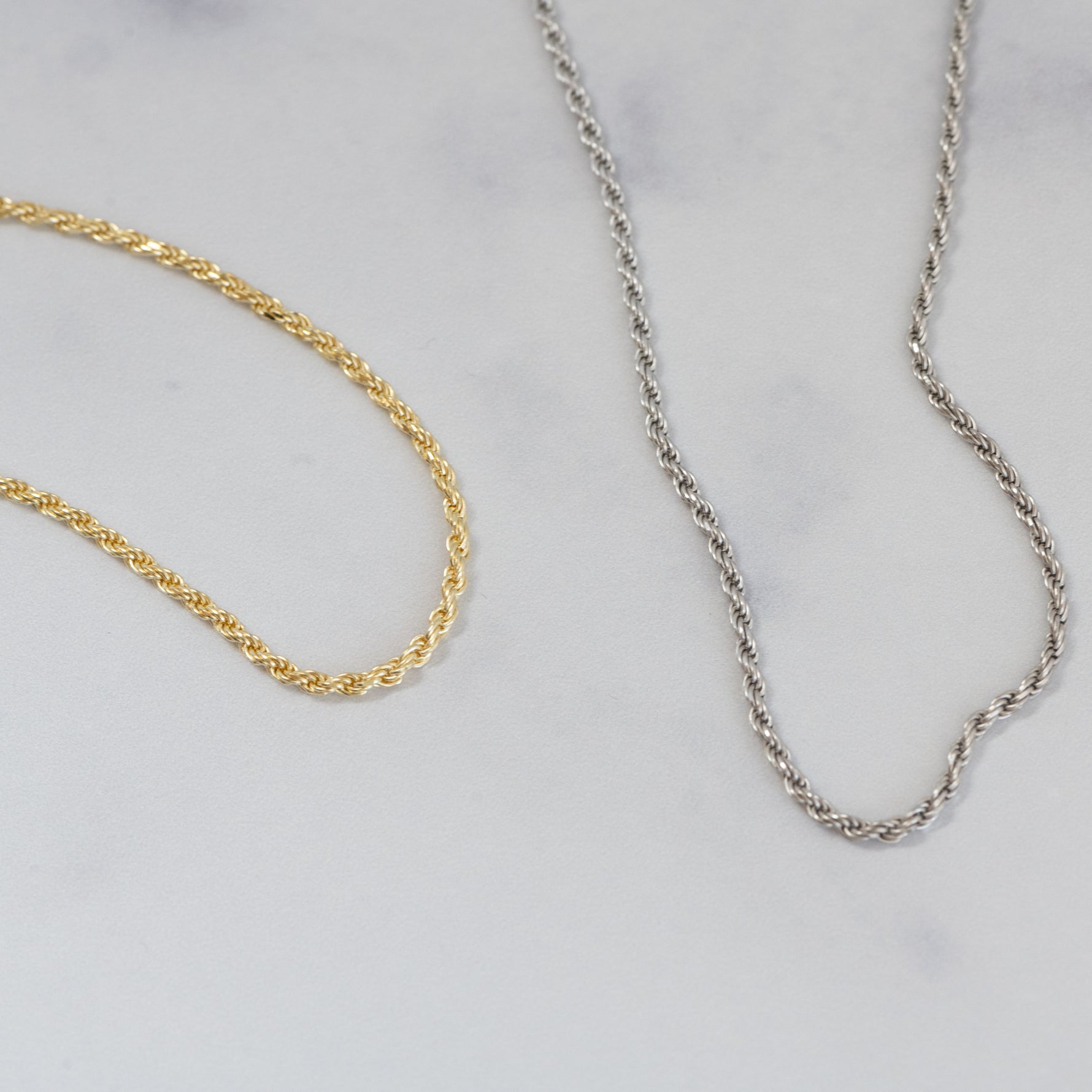 Gold and silver dainty thin rope chain necklaces on a marble background.