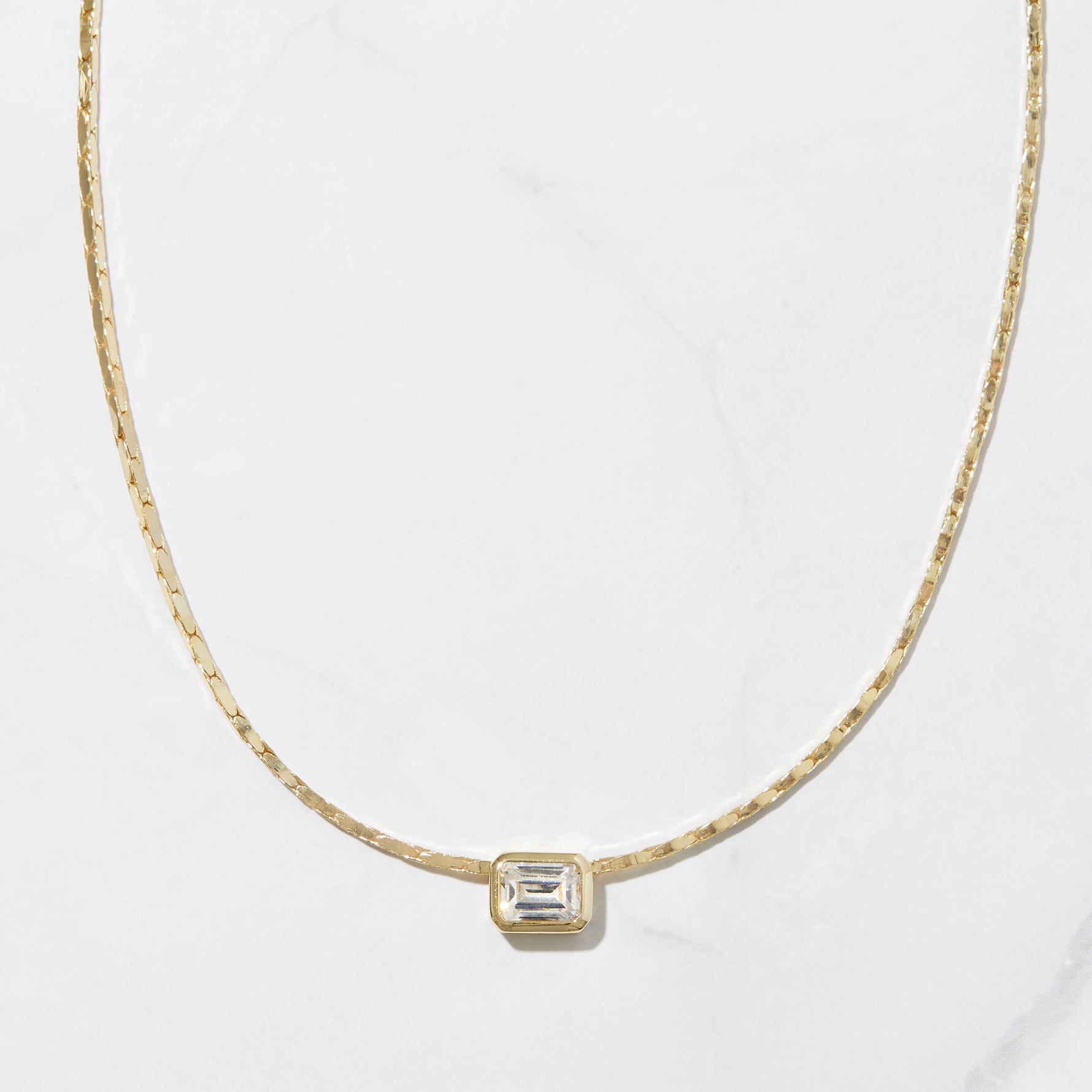 Gold statement baguette bezel pendant necklace on marble background