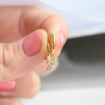 Model holding dainty gold diamond bezel huggie earrings. 