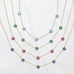 Gold dainty birthstone flower charm necklaces on a marble background.