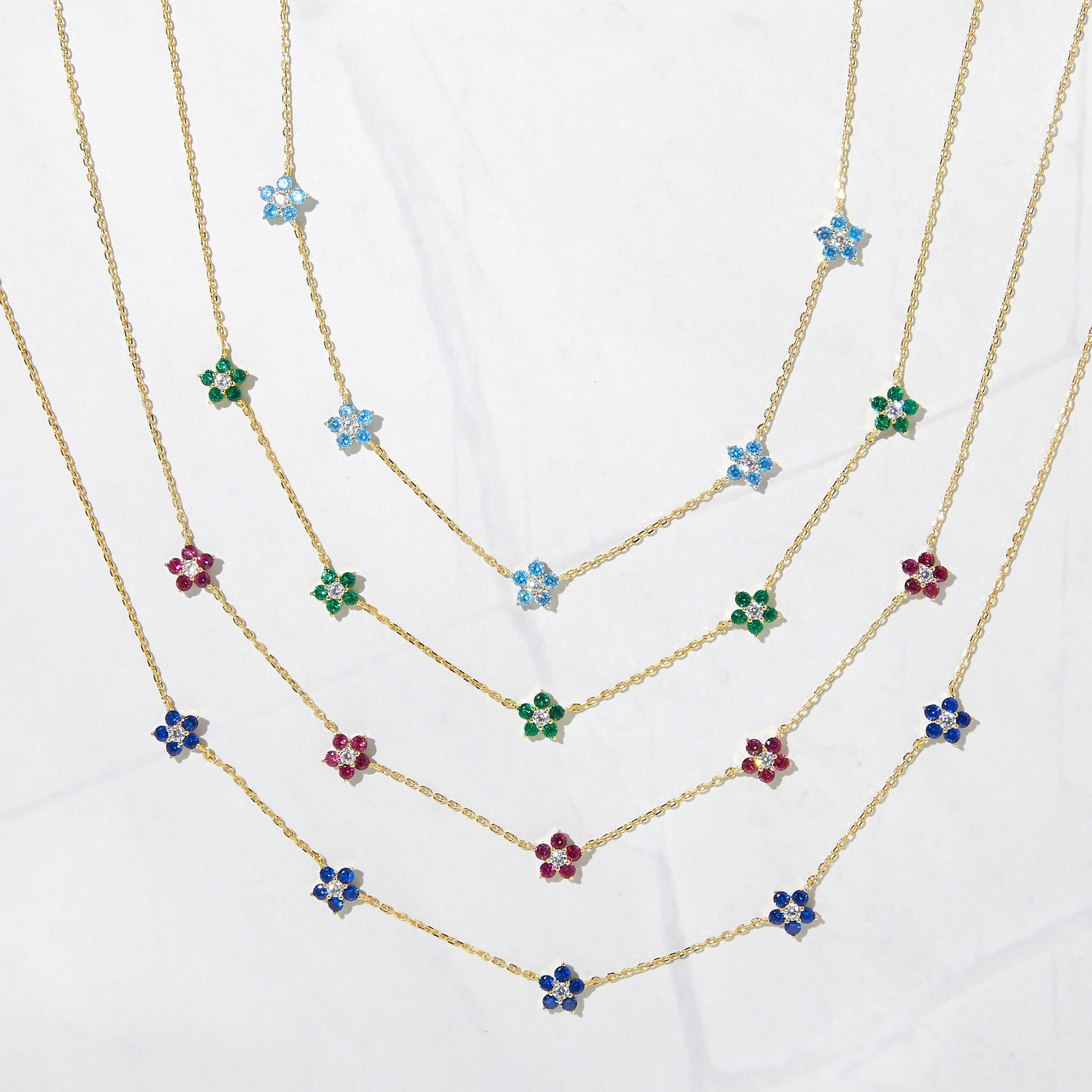 Gold dainty birthstone flower charm necklaces on a marble background.