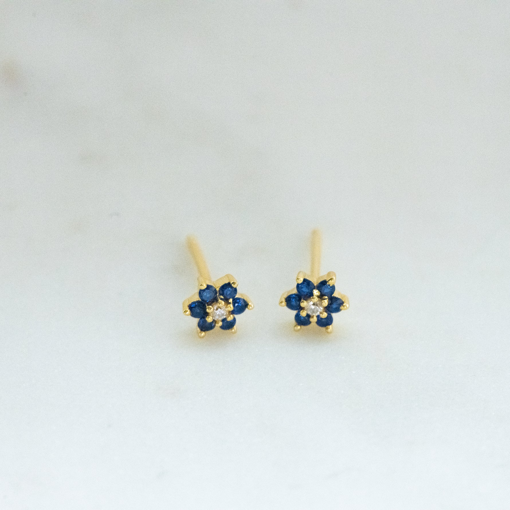 Upclose shot of gold flower stud earrings with sapphire birthstone.