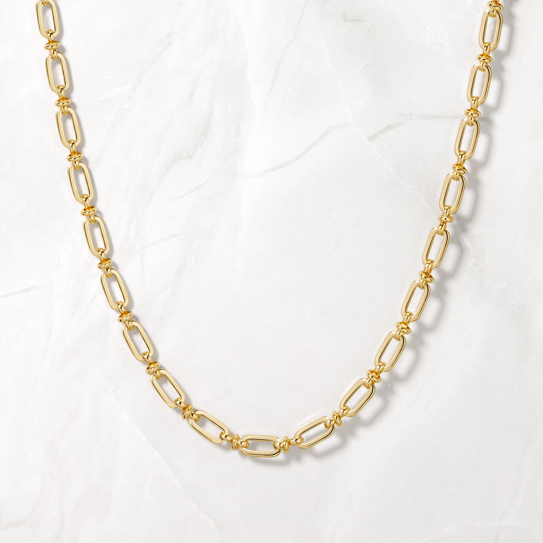 Trendy gold chain link statement necklace on marble background.