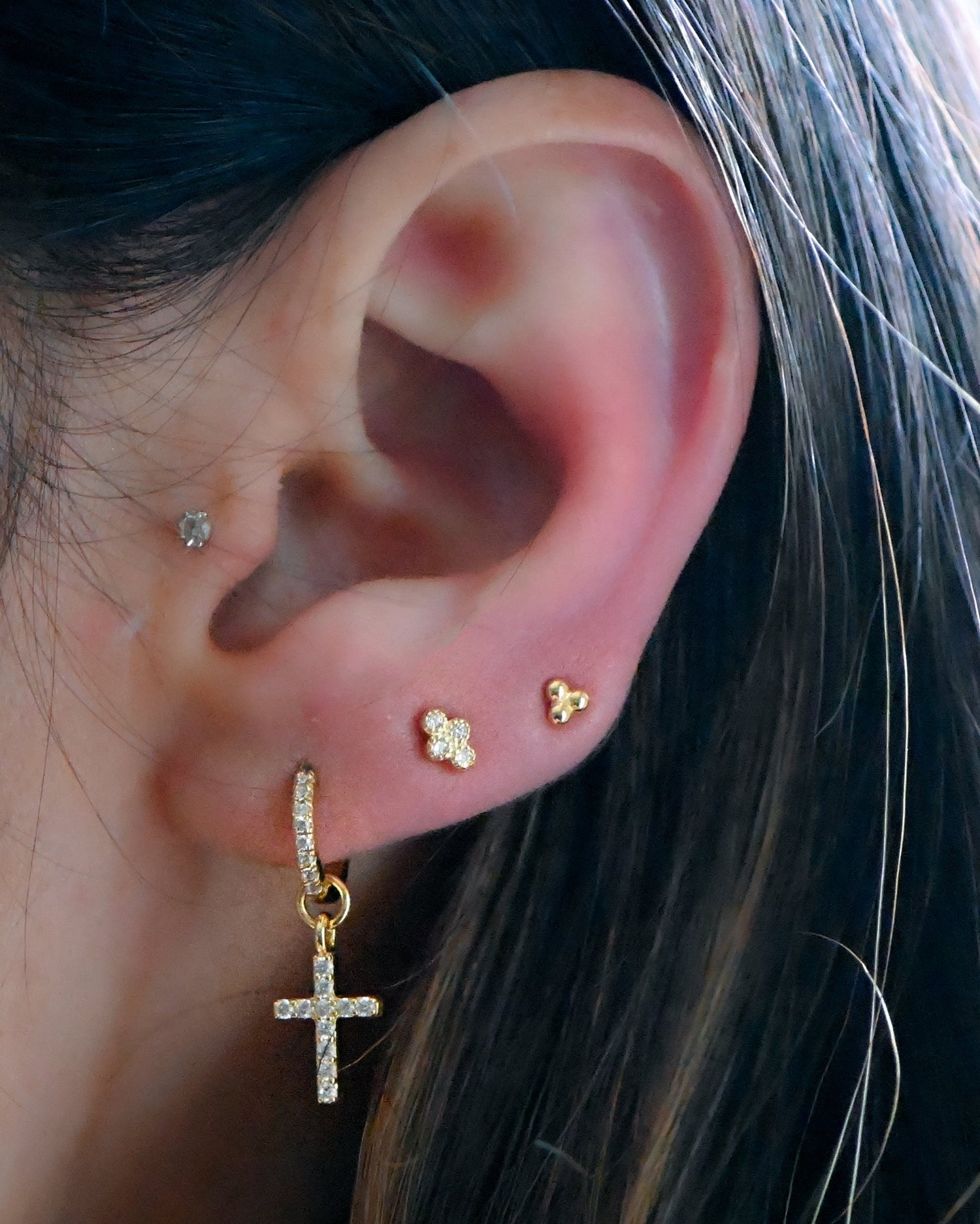Model wearing gold cross charm earrings with gold cz and plain ball stud earrings.