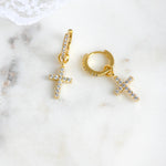 Delicate gold diamond cross huggies on marble background