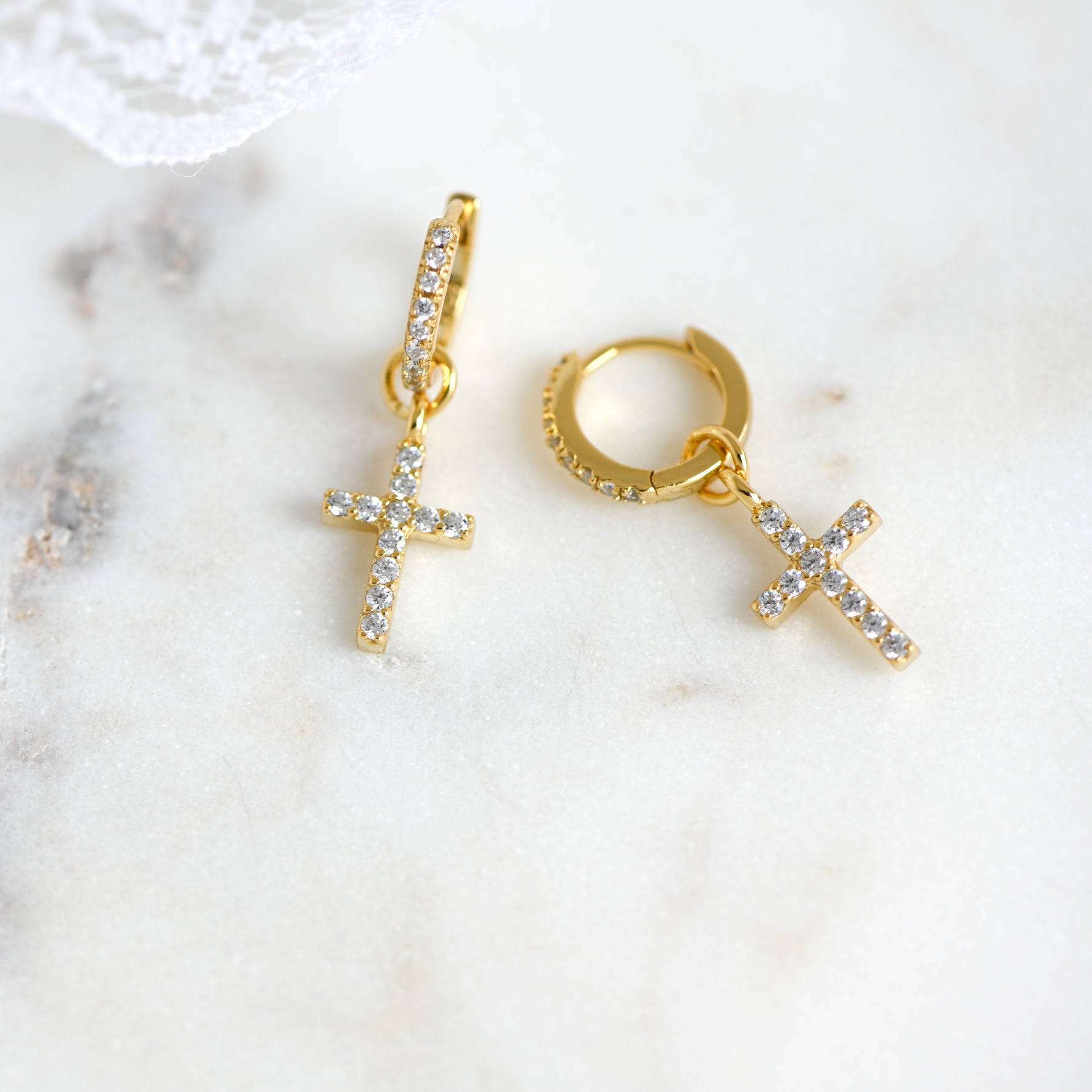 Delicate gold diamond cross huggies on marble background