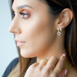 Model wearing pavé feminine gold earring stack including a diamond stud, a diamond huggie, and a heart charm diamond hoop.