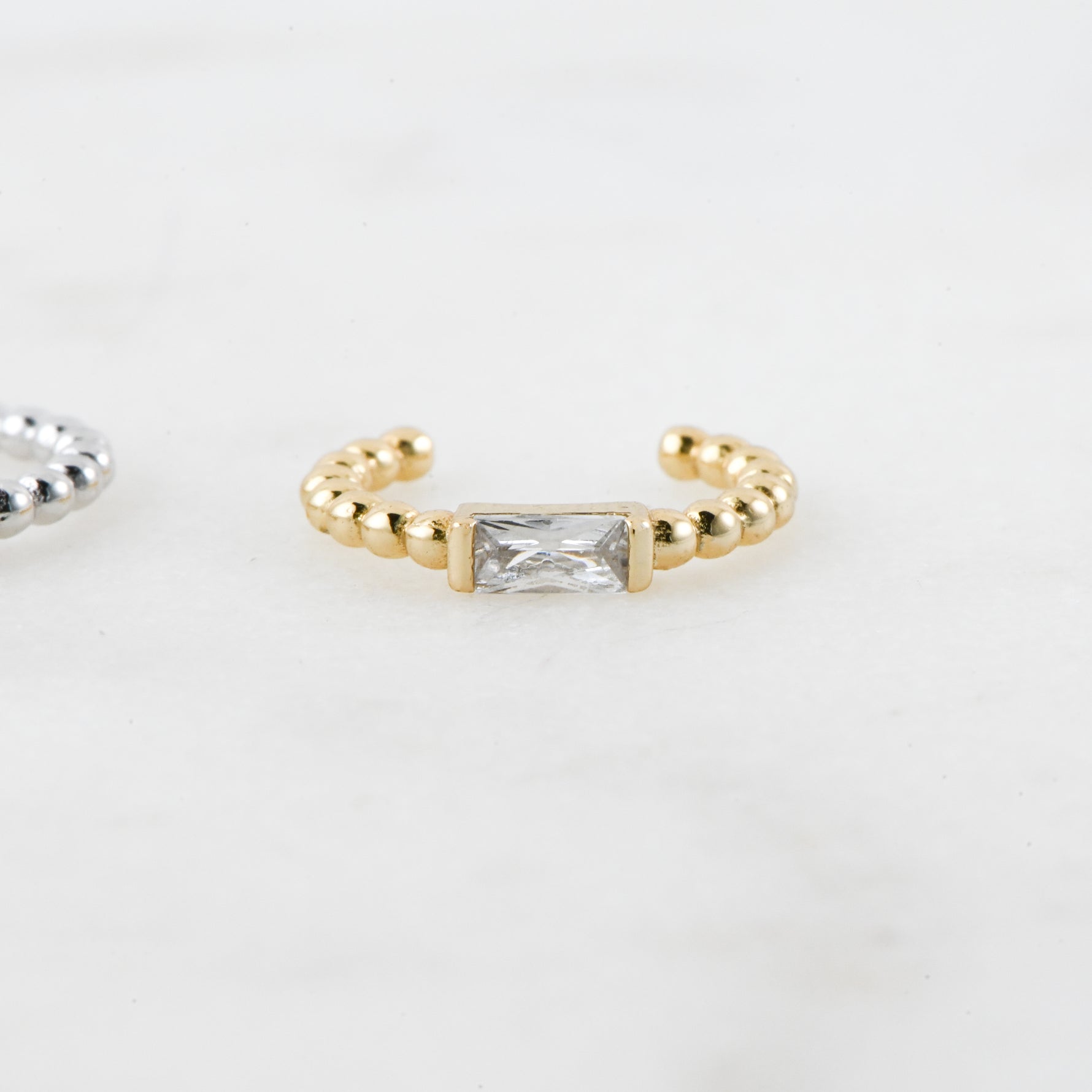 Gold beaded baguette gemstone ear cuff on plain background.