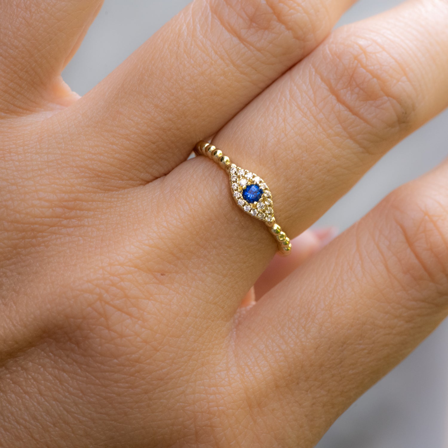 Model wearing delicate gold beaded evil eye stacking ring. 