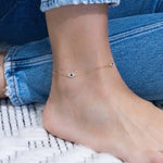 Model wearing summery gold evil eye cz and sapphire charm ankle bracelet