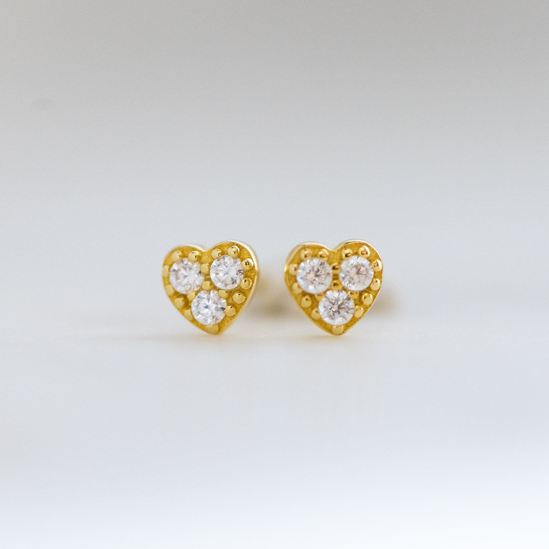 Closeup image of dainty heart cz studded earrings on plain background.