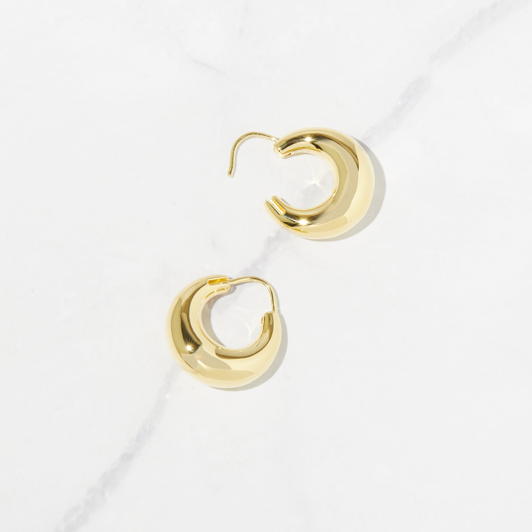 Closeup image of basket gold hoop earrings from the side showing the clasp opening on a marble background.