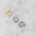 Gold and silver cz diamond studded huggie earrings on a marble background.