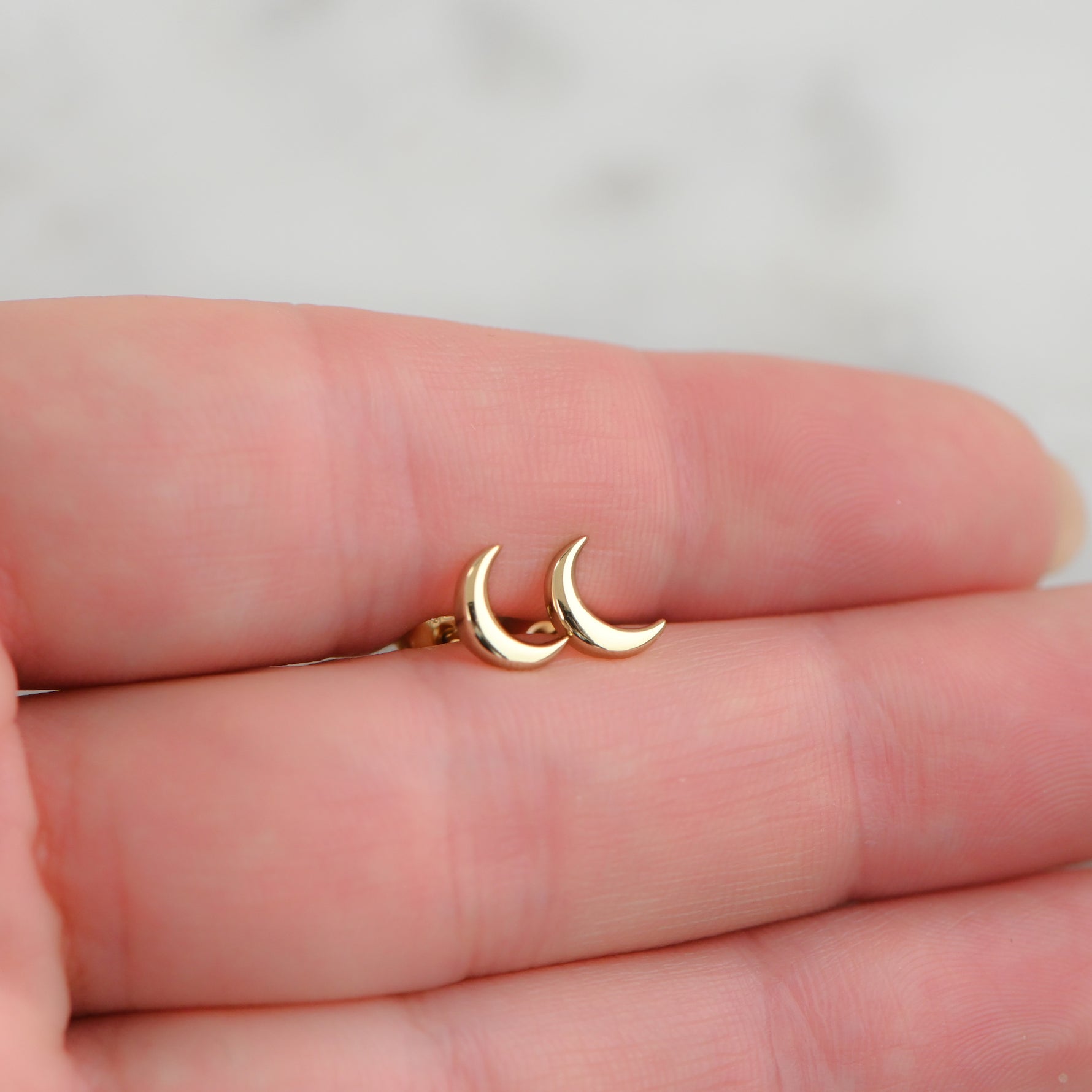Model holding delicate gold plain moon stud earrings