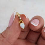 Dainty gold opal charm huggie hoops in model's hand.