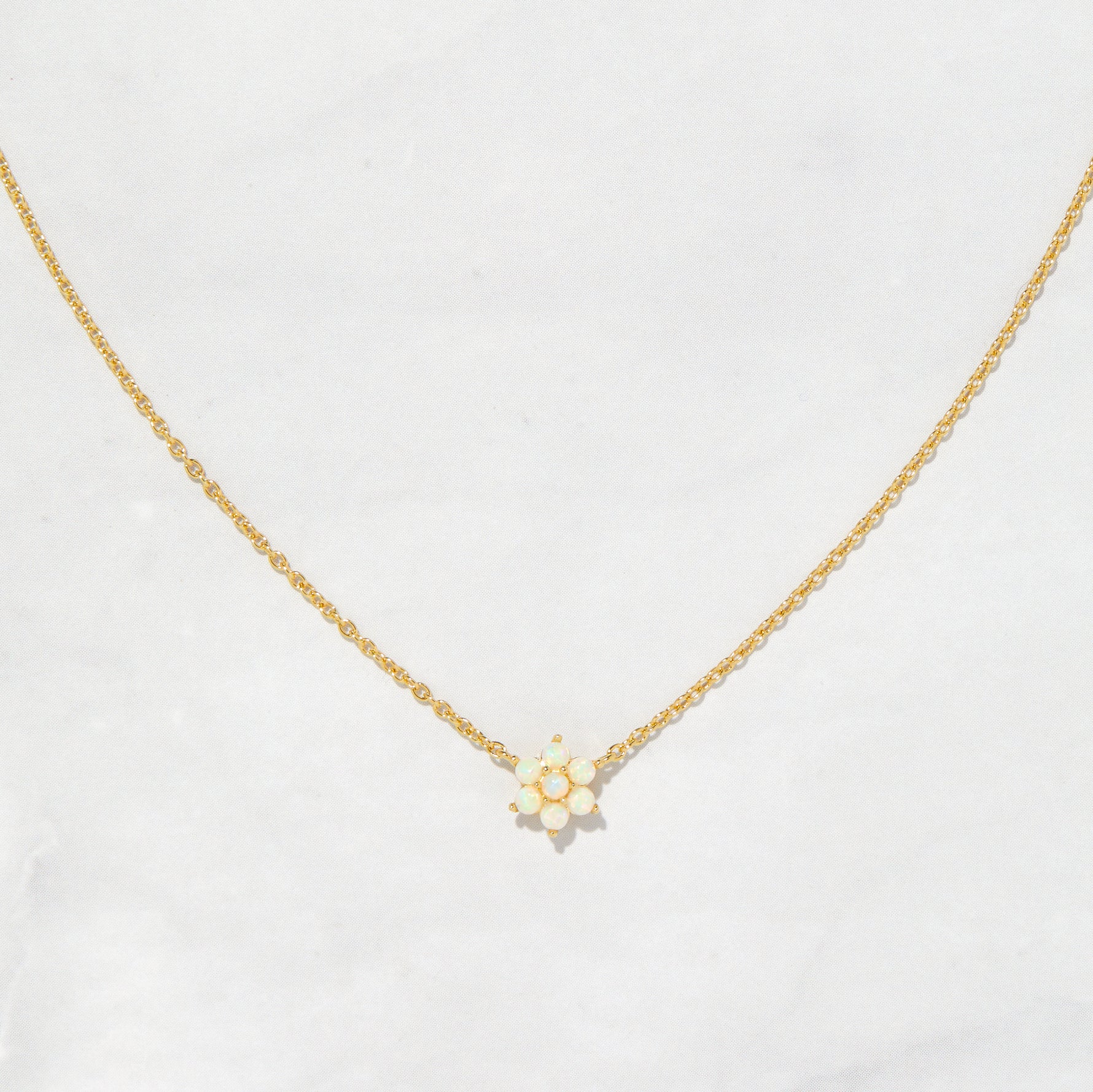Gold opal flower pendant necklace on plain background
