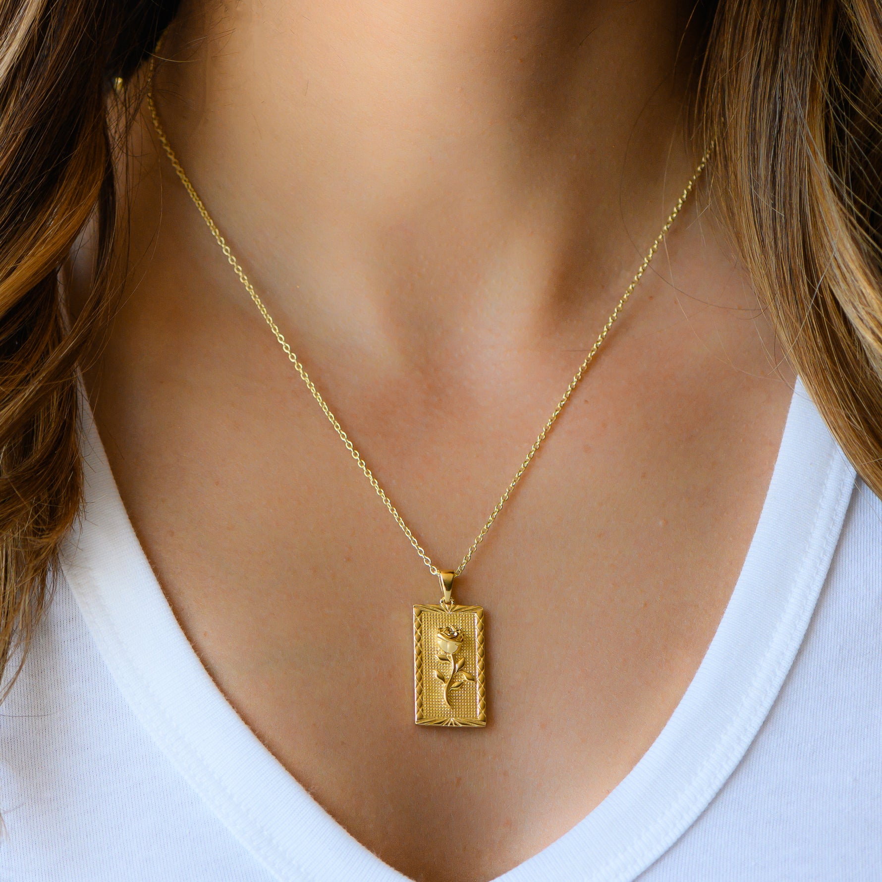 Model wearing gold rectangle rose medallion necklace.