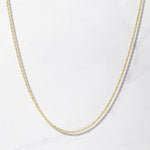 Thin gold rope chain necklace on plain marble background