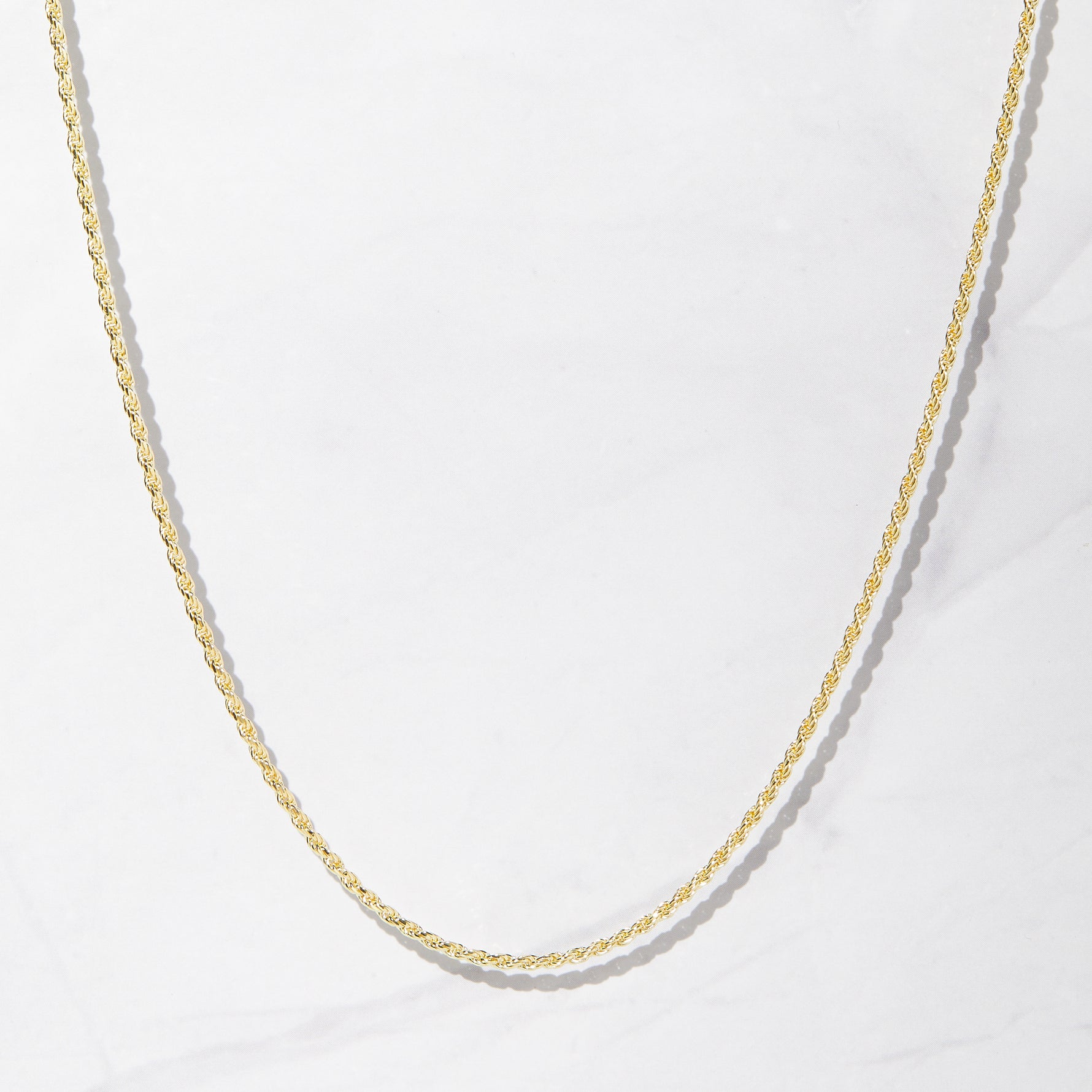 Thin gold rope chain necklace on plain marble background