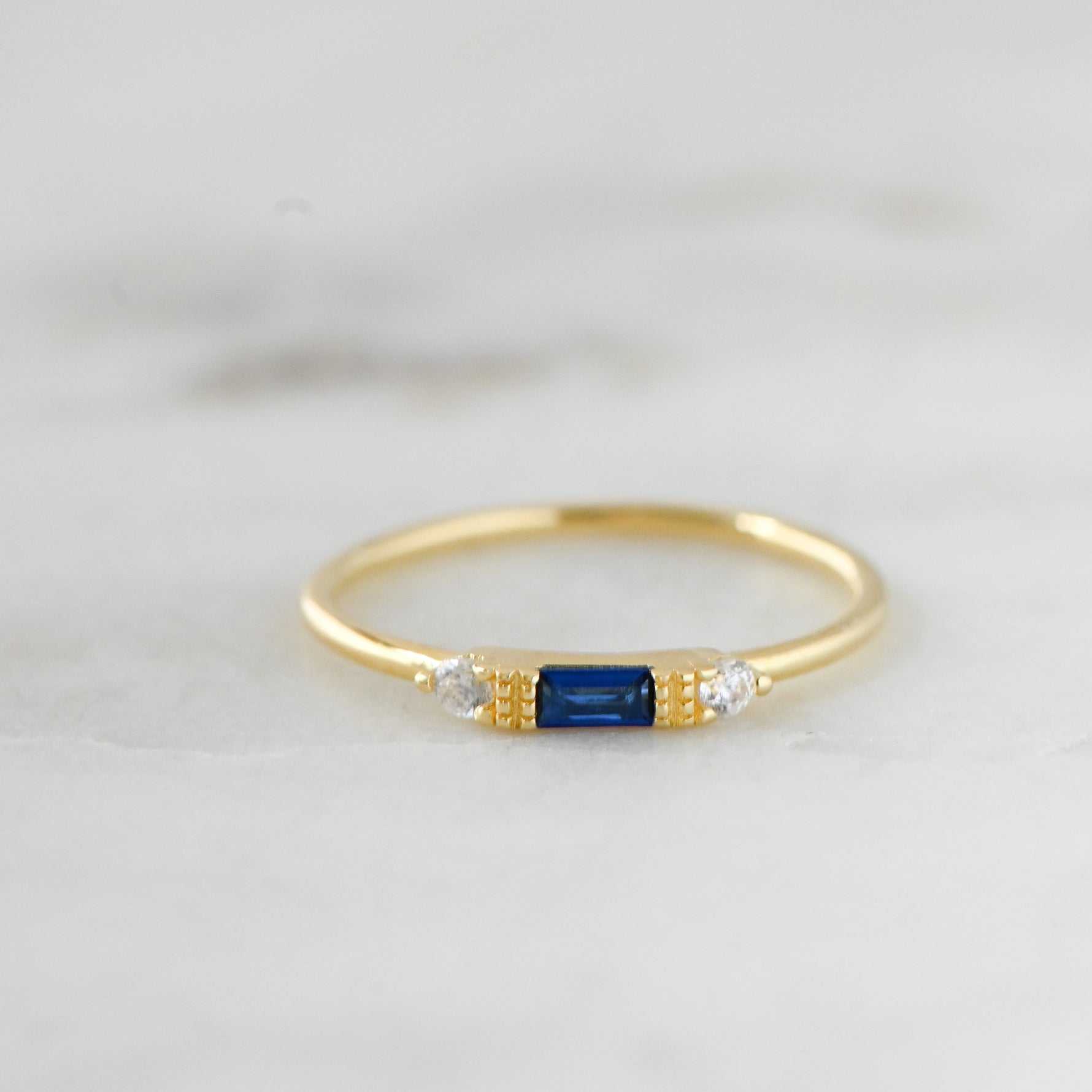 Dainty gold birthstone sapphire ring on marble background. 