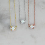 Close-up of opal halo necklace in gold, silver, and rose gold on marble background.