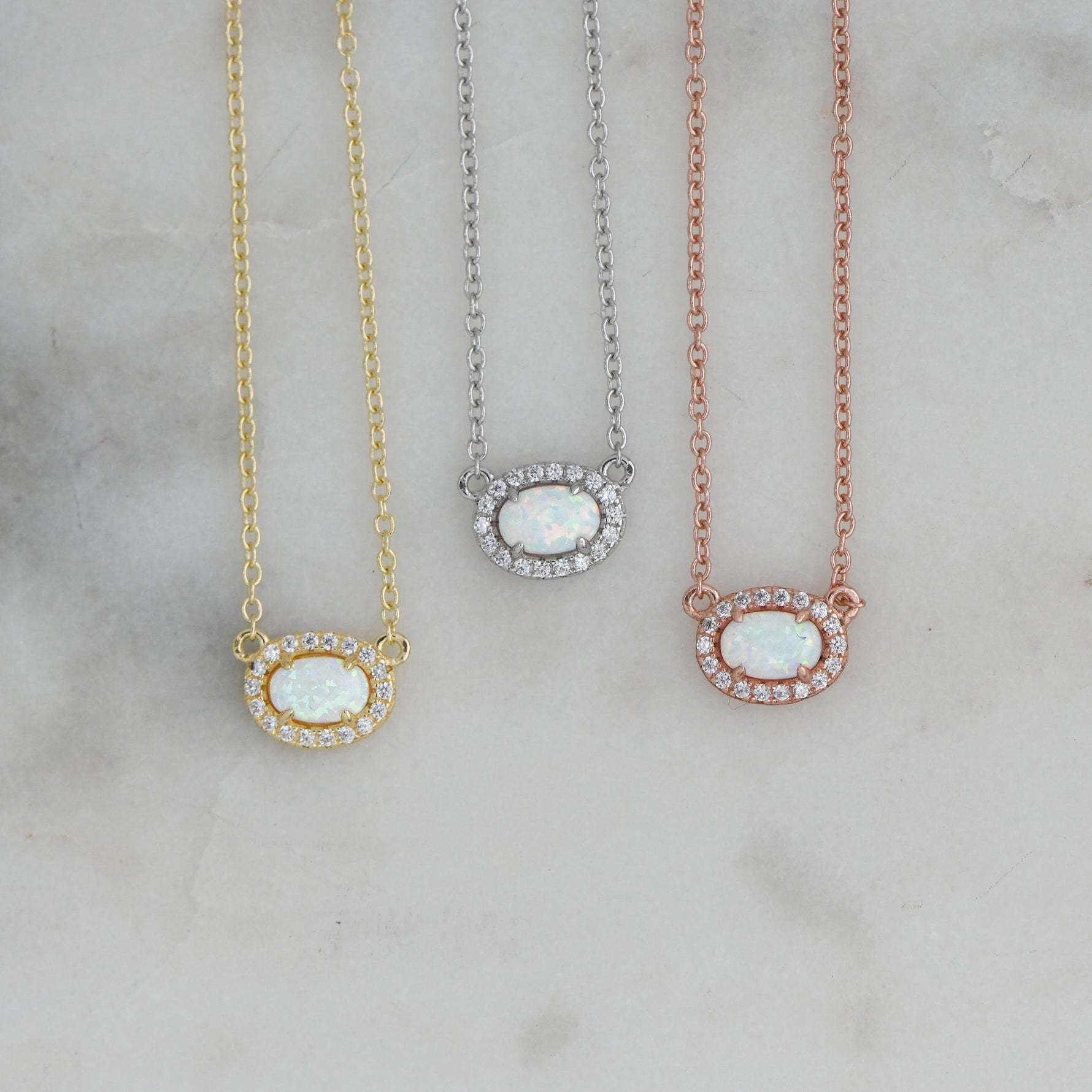 Close-up of opal halo necklace in gold, silver, and rose gold on marble background.