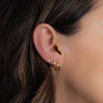 Model wearing minimalist gold double hoops with plain huggies and tiny baguette studs.