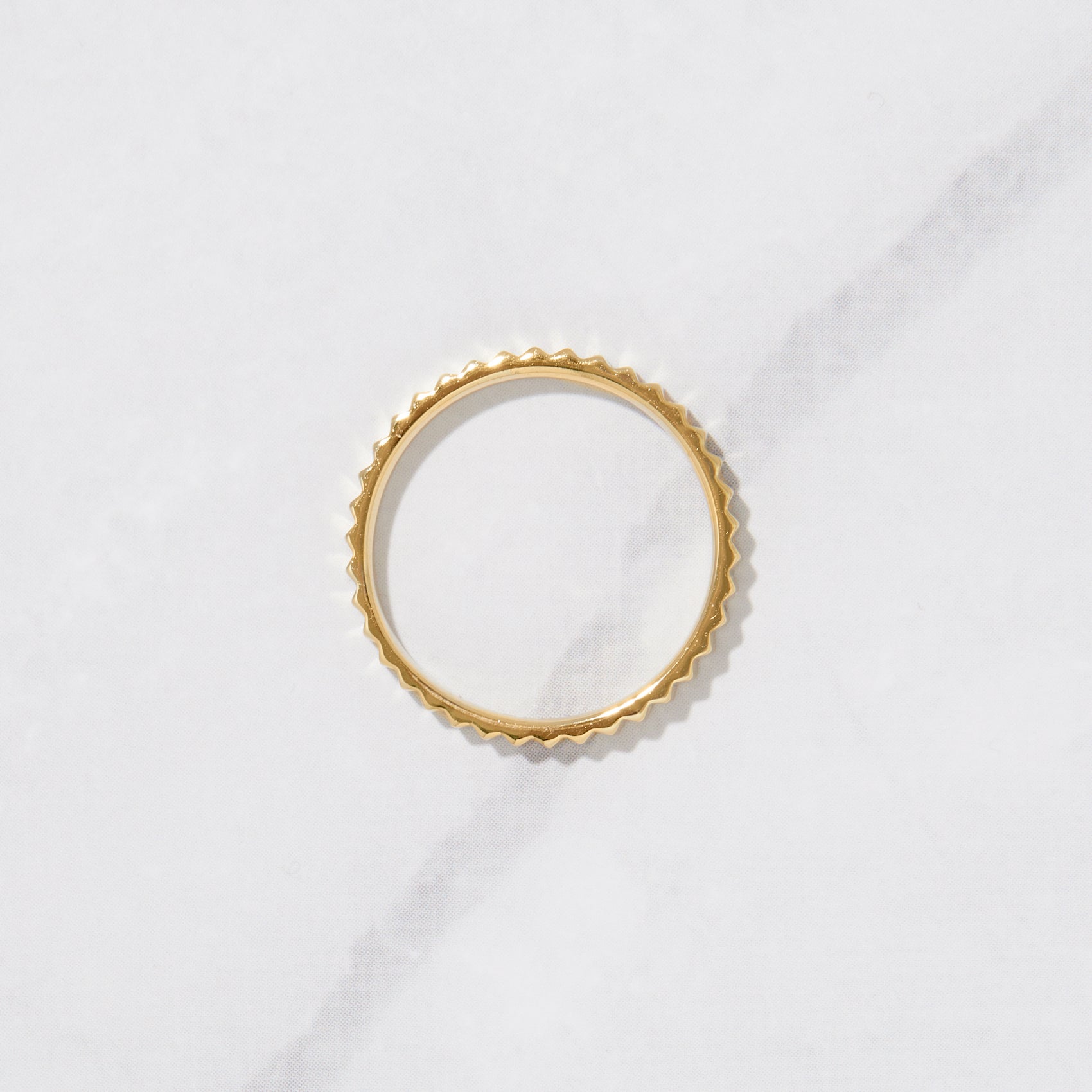 Textured gold ring from the side on a marble background. 