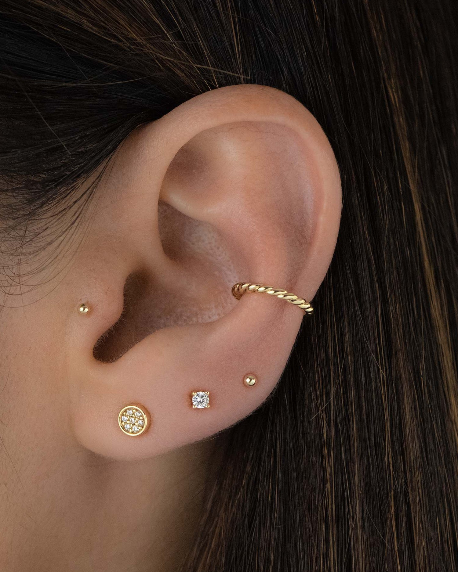 Model wearing minimalist gold stud earrings stacked with a spiral ear cuff 