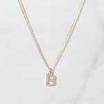 Gold studded letter necklace on marble background