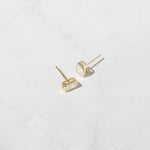 Gold baguette stud earrings on marble background. 