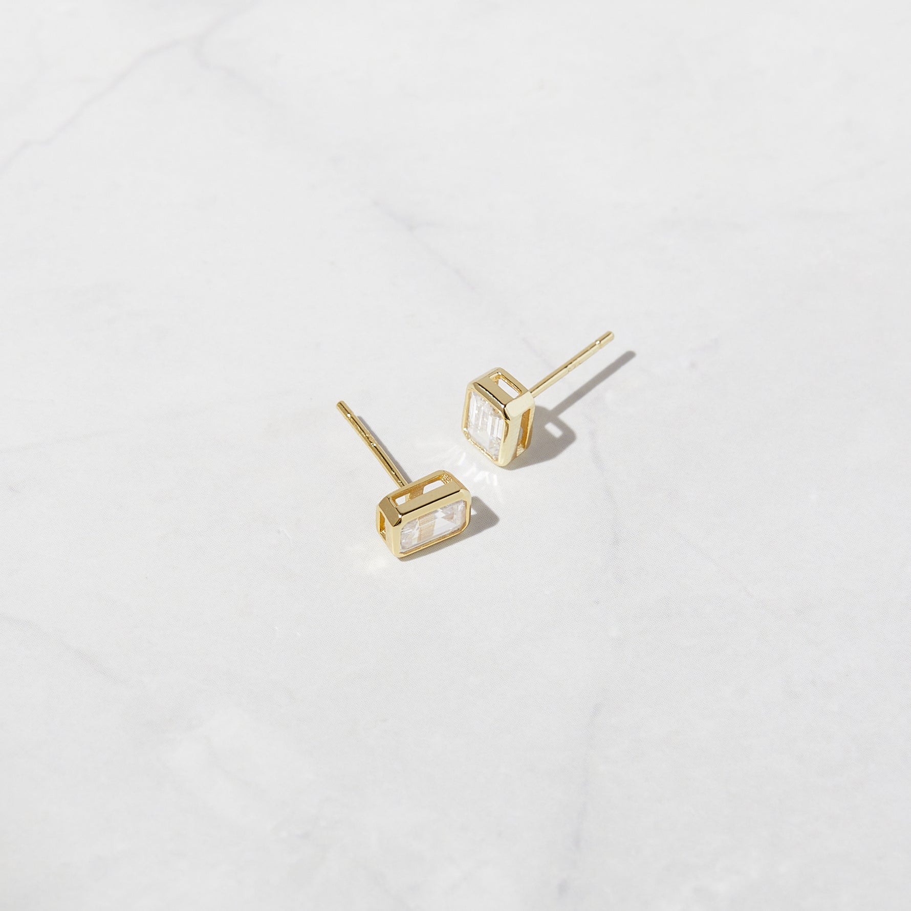 Gold baguette stud earrings on marble background. 