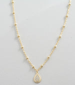 Up-close of gold pavé tear drop pendant necklace on a beaded chain. 