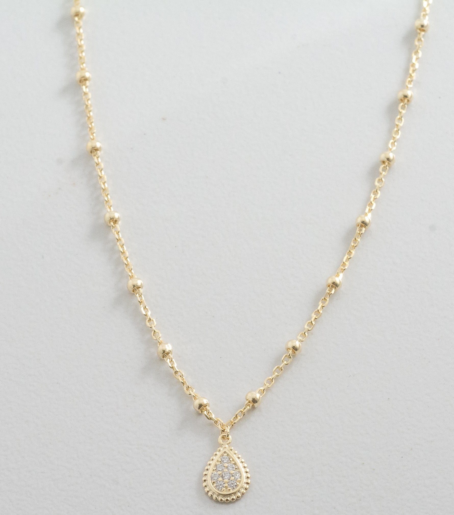 Up-close of gold pavé tear drop pendant necklace on a beaded chain. 
