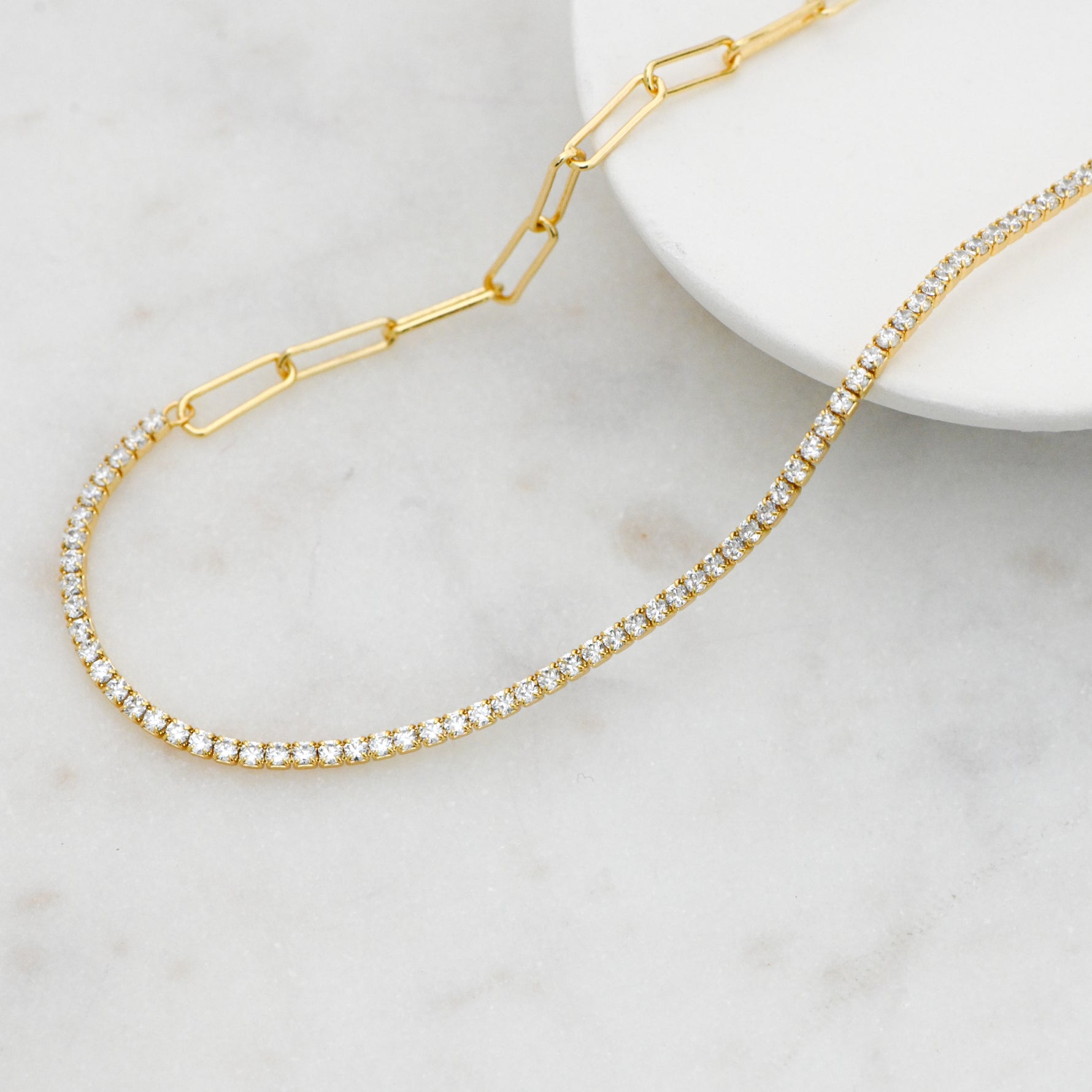 Gold tennis and paperclip chain necklace on marble background. 