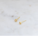 Tiny gold heart stud earrings from the side angle on marble background.