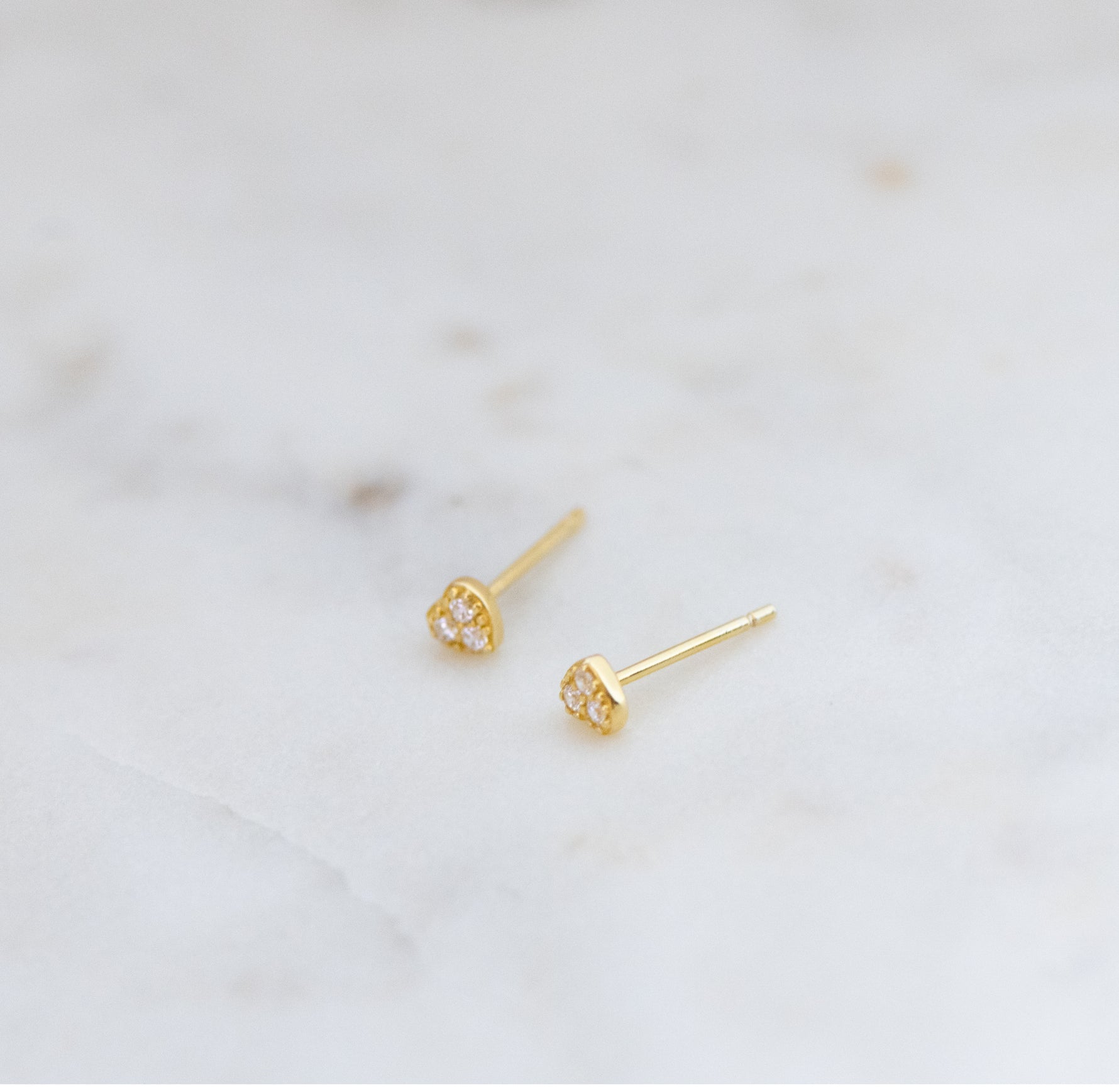 Tiny gold heart stud earrings from the side angle on marble background.