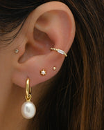 Model wearing gold pearl charm earrings, dainty pearl studs, ball studs, and a cz baguette ear cuff. 