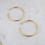 Closeup of oversized large gold hoop earrings on marble background.