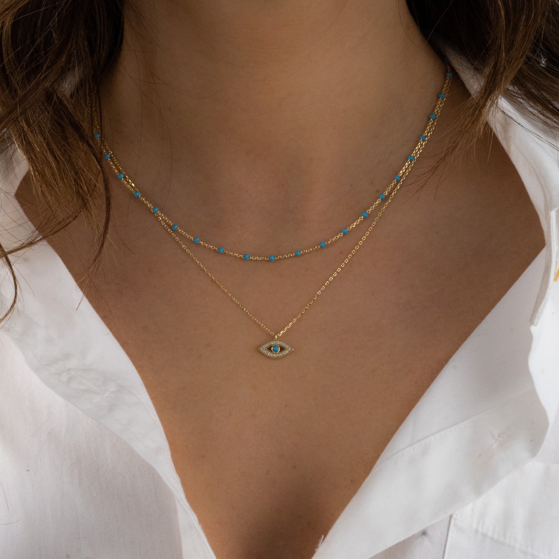 Model wearing delicate gold turquoise beaded necklace layered with a turquoise evil eye necklace. 