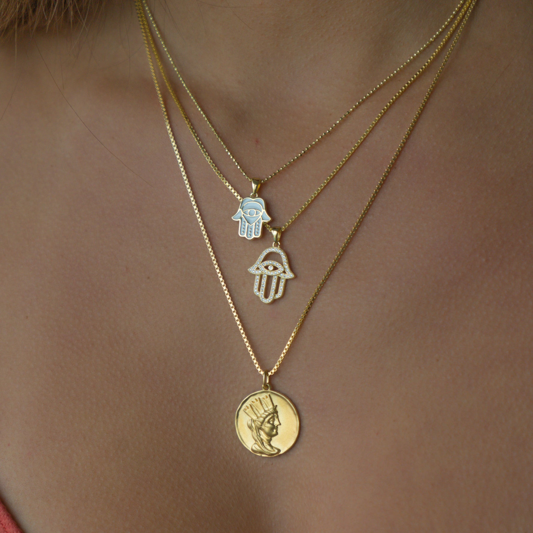 Gold hamsa necklace in a stack of three gold layered pendant necklaces. 