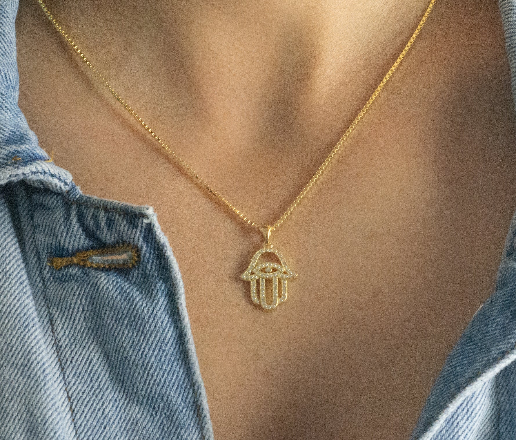 Model wearing gold statement hamsa pendant necklace. 