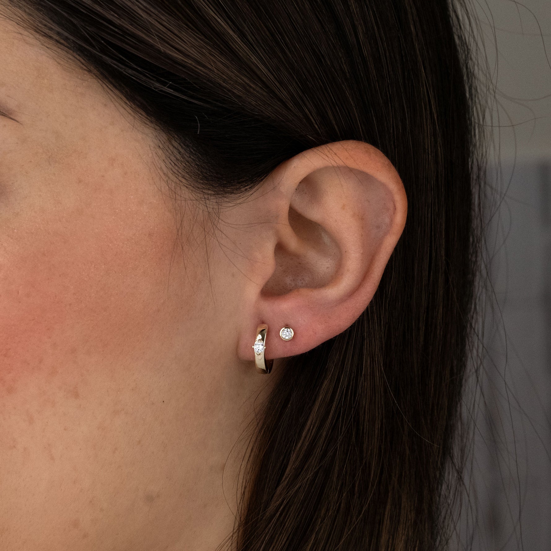 Model wearing gold huggie hoops and bezel studs