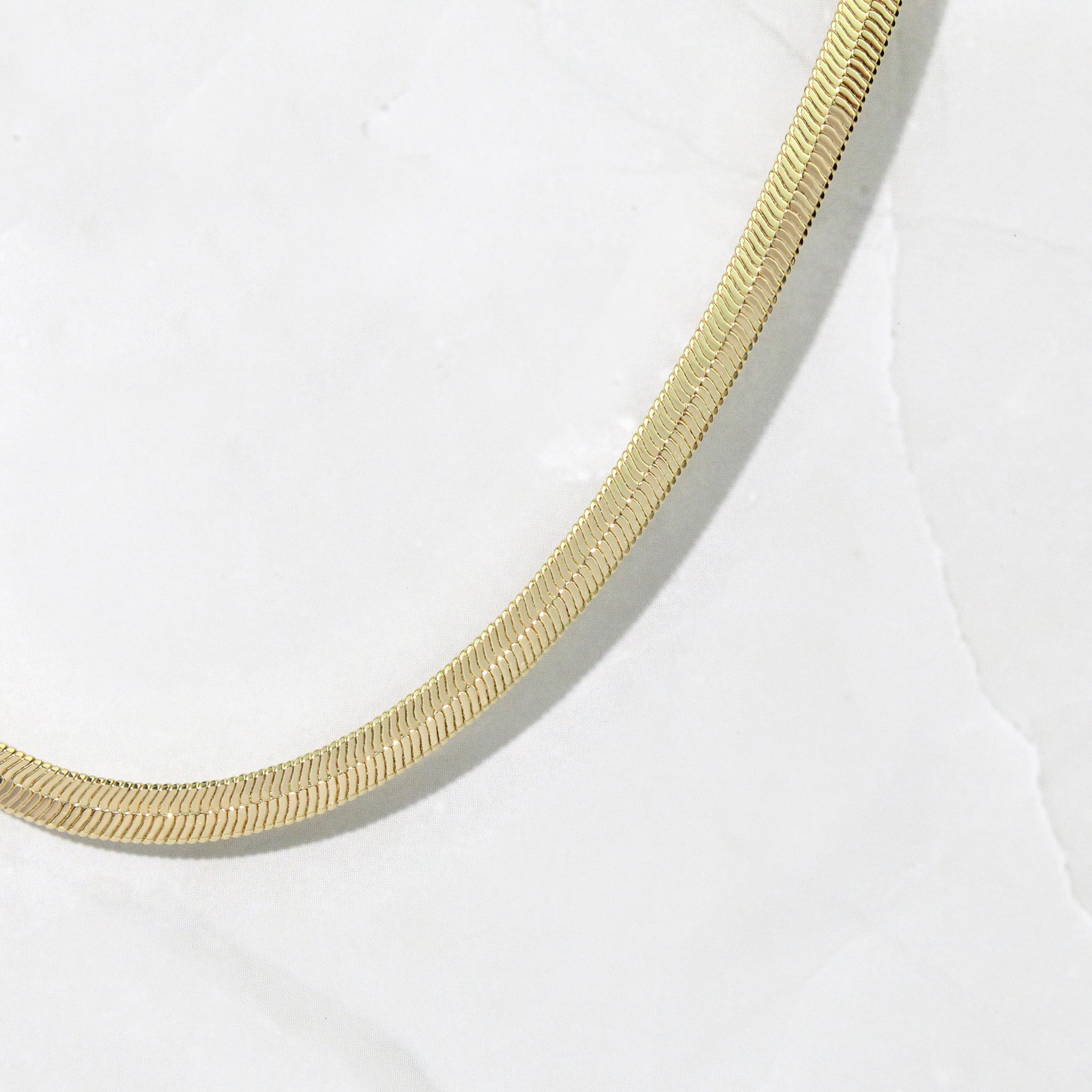 Upclose shot of a gold minimalist herringbone chain necklace.