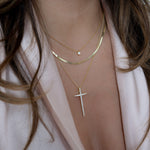 Model wearing gold cross layering necklace with herringbone chain and tiny bezel pendant necklace.