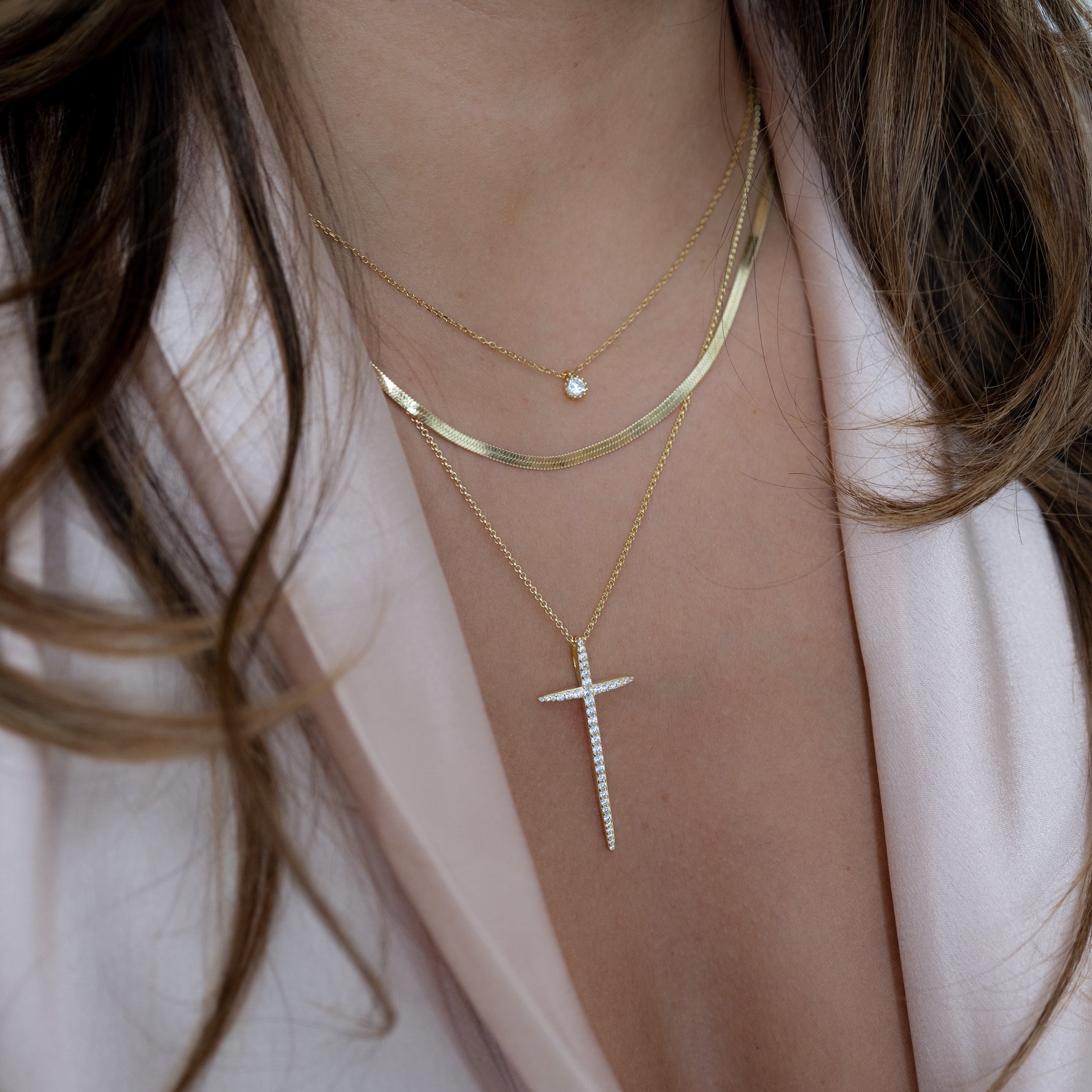 Model wearing gold cross layering necklace with herringbone chain and tiny bezel pendant necklace.