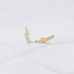 Delicate gold studded lightning bolt earrings on marble background. 