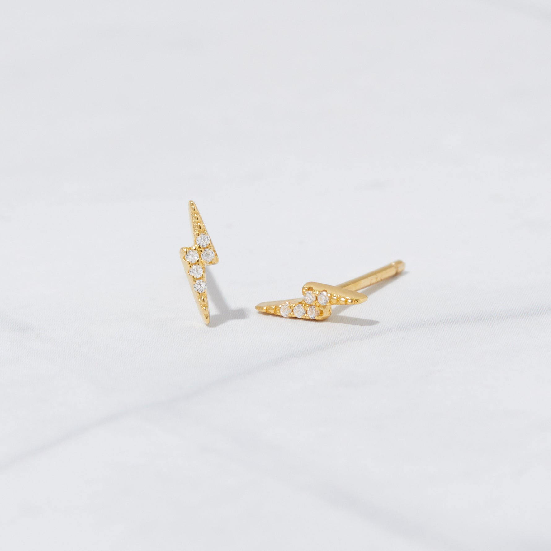 Delicate gold studded lightning bolt earrings on marble background. 