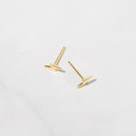 Delicate gold plain lightning bolt stud earrings on white marble background. 